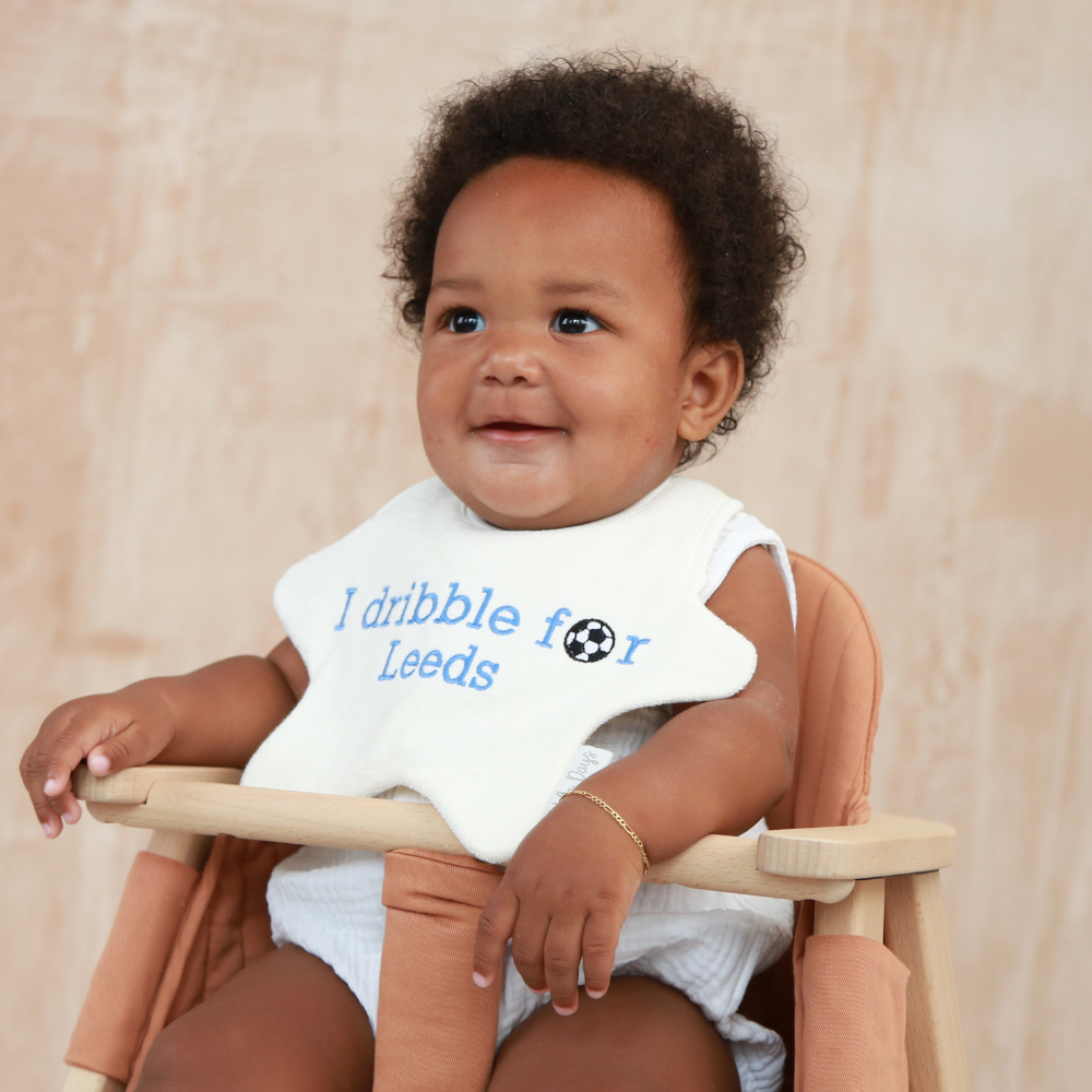 Baby wearing a cream, star shaped bib with 'I dribble for Leeds' embroidered on