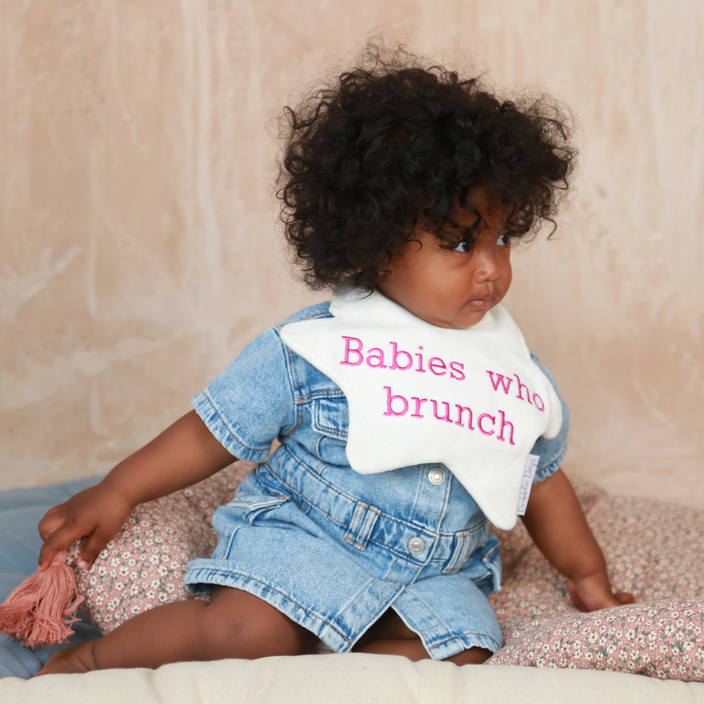 Baby wearing a star shaped bib with 'Babies who Brunch' embroidered on
