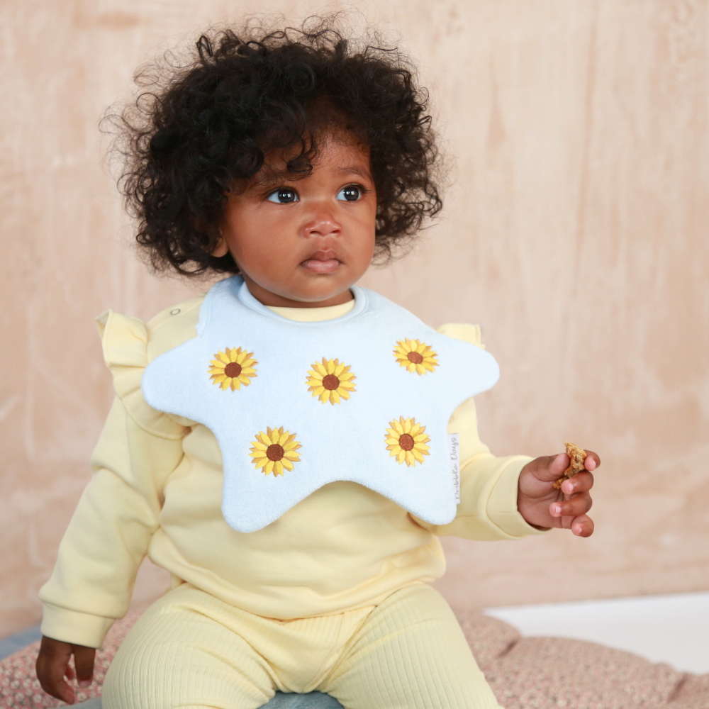 Baby wearing a star shaped bib with embroidered yellow sunflowers