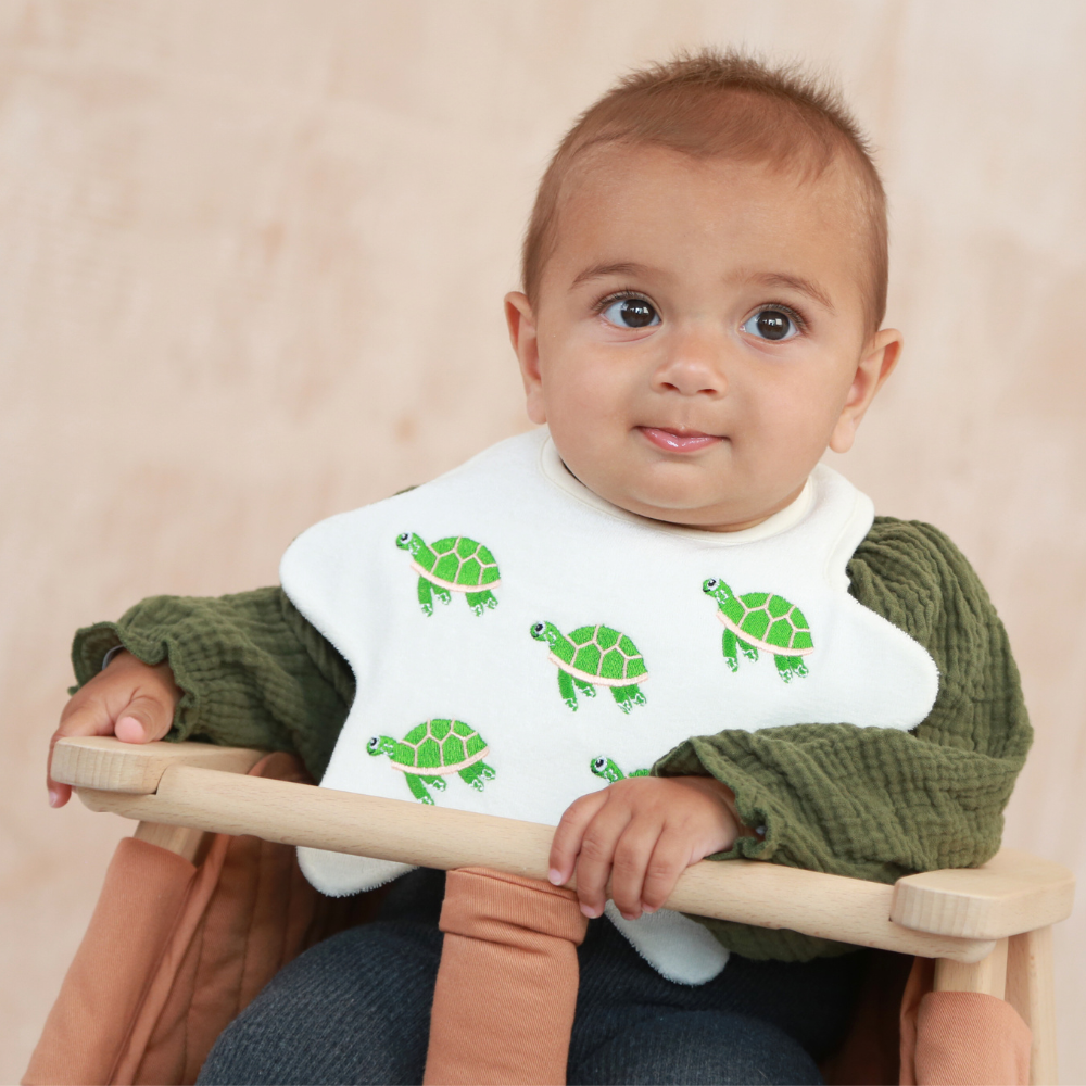 Baby wearing a star shaped bib with embroidered turtles