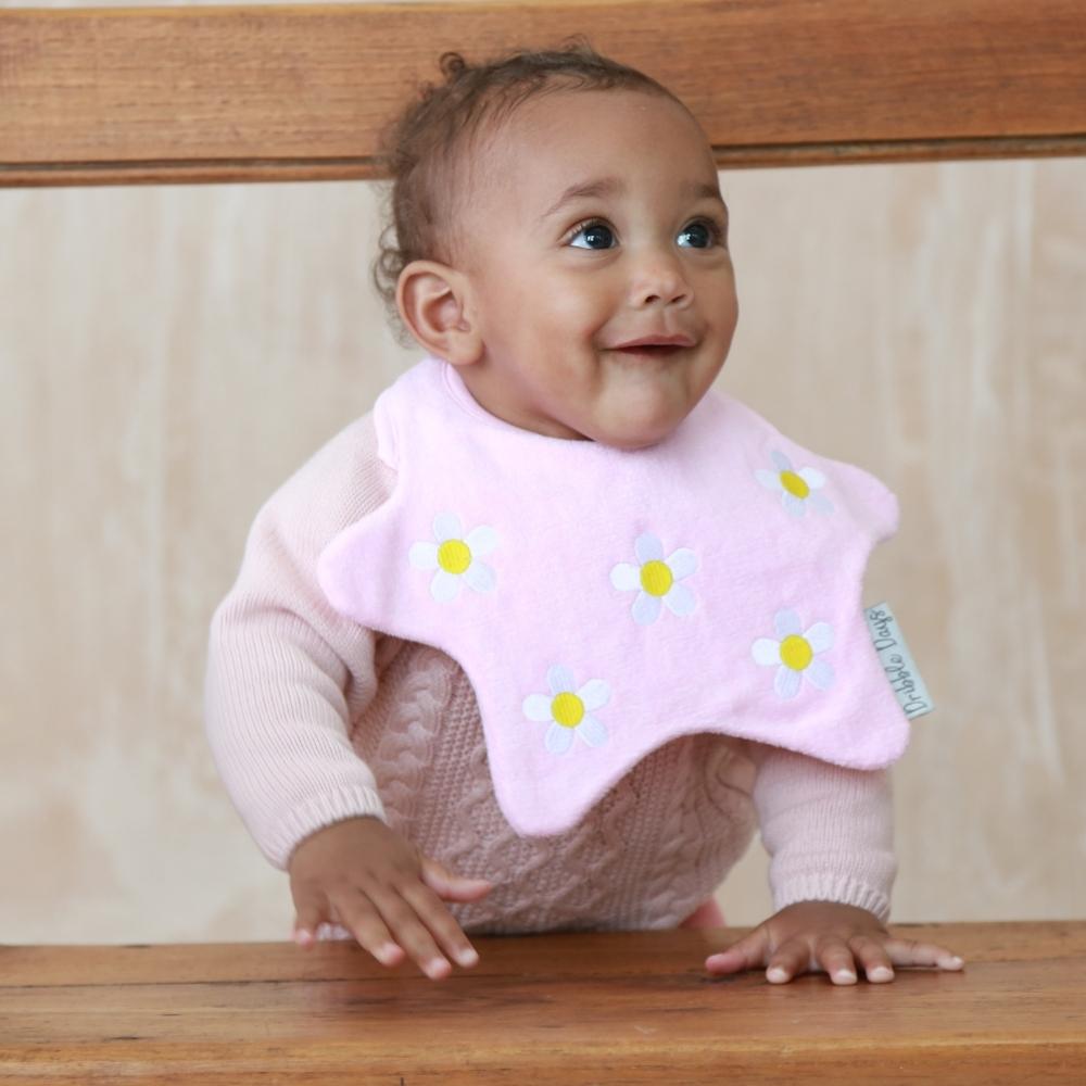 Baby standing with towelling pink daisy bib