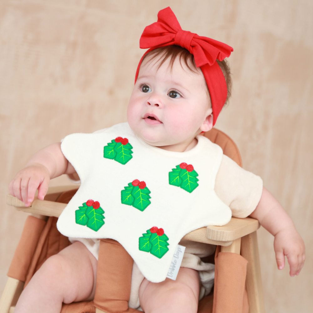 Baby wearing a star shaped bib with embroidered Christmas Hollies