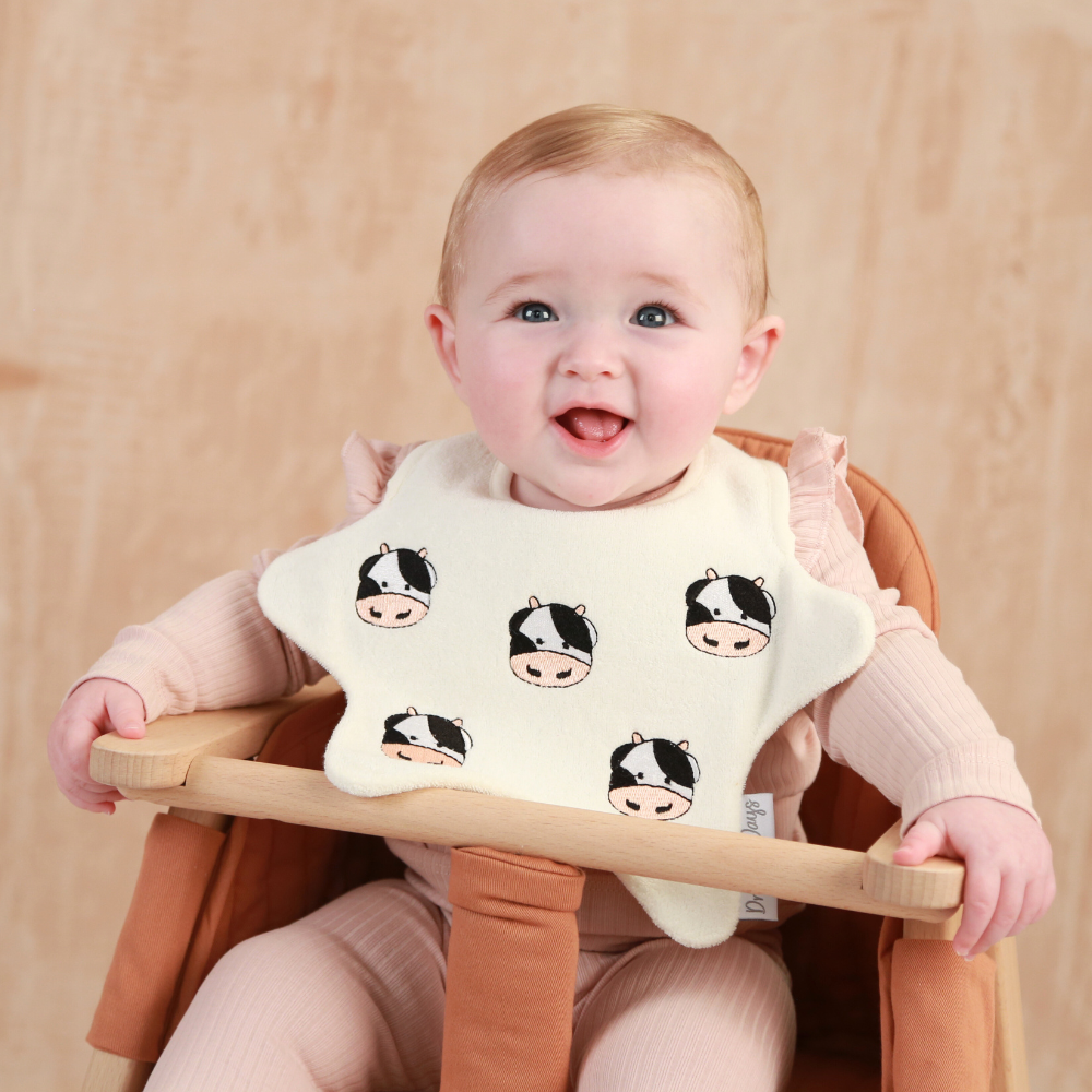 Baby wearing a star shaped bib with embroidered Cows