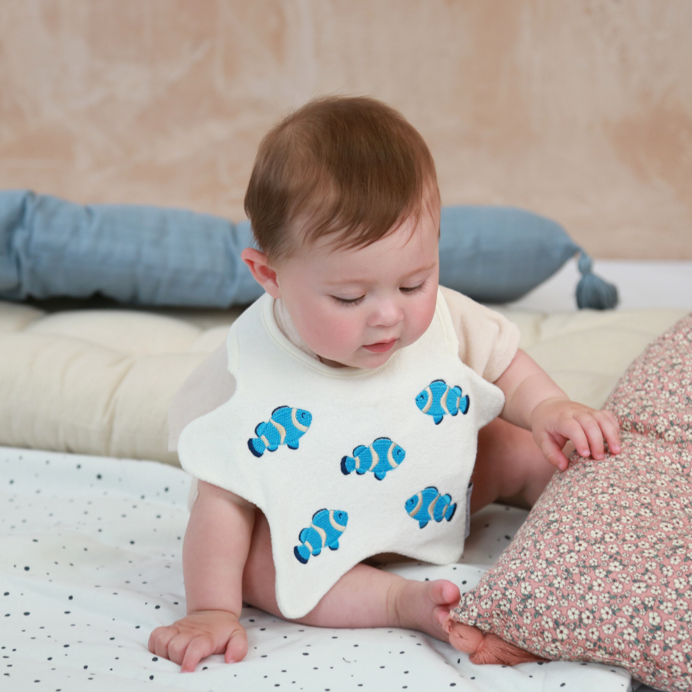 Baby wearing a star shaped bib with embroidered blue and white fish