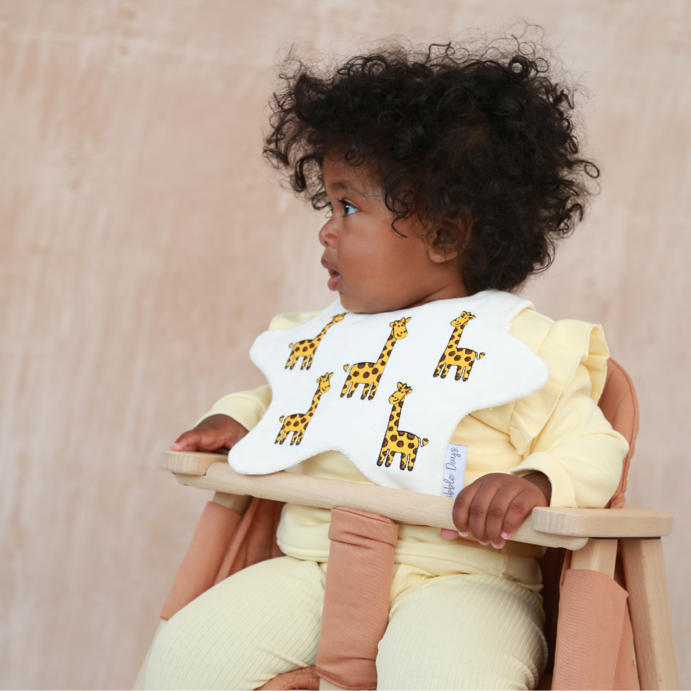 Baby wearing a cream, star shaped bib with embroidered Giraffes