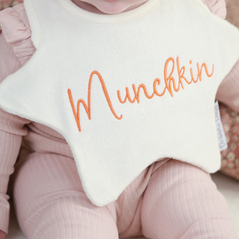 Baby wearing a star shaped bib with 'Munchkin' embroidered on