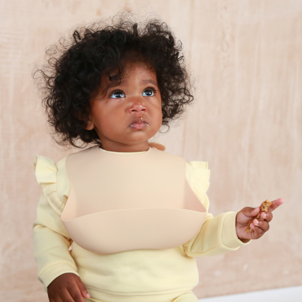 Baby wearing a beige, neutral coloured silicone feeding bib