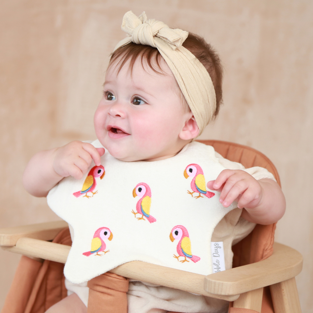 Baby wearing a star shaped bib with embroidered Pink and Yellow Parrots