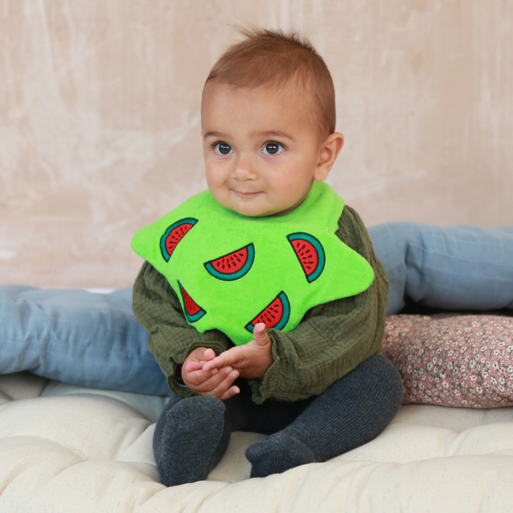 Baby wearing a green, star shaped bib with embroidered watermelons